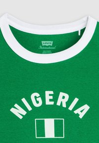 Πράσινο T-shirt με λευκό γιακά που φέρει το κείμενο «NIGERIA» και τύπωμα της σημαίας της Νιγηρίας, με ετικέτα Levi's International στο εσωτερικό του γιακά.