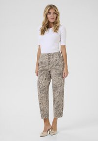 Pantalon droit en motif léopard beige avec des taches noires, doté d'une taille haute et de poches latérales. Associé à un haut blanc ajusté.