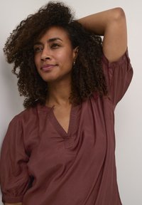 Bordeauxfarbige Bluse aus leichtem Stoff, mit V-Ausschnitt, gerafften kurzen Ärmeln und einem entspannten Schnitt mit weicher Textur.