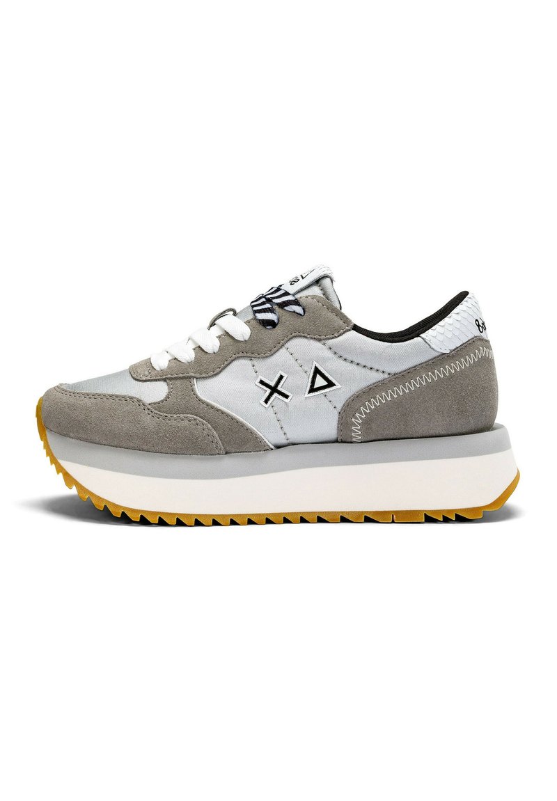 Zapatilla gris y blanca con materiales de gamuza y tela, que presenta detalles en negro, una suela texturizada y diseños geométricos en los laterales.