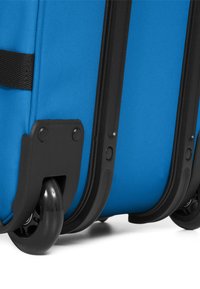 Blauwe stoffen koffer met zwarte kunststof frame, voorzien van vier wielen en getextureerde accenten aan de zijkanten voor grip en duurzaamheid.