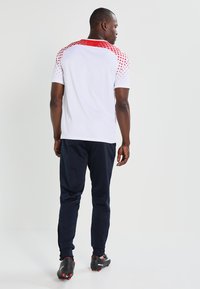 Witte sportieve shirt met rode stippen op de schouders en marineblauwe broek. Voorzien van een relaxte pasvorm en korte mouwen, ideaal voor sportkleding.