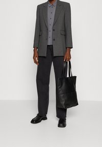 Blazer gris con hombros estructurados sobre una camisa abotonada, pantalones negros de pierna recta, bolso tote de cuero negro y zapatos negros.