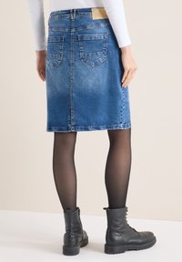 Jupe en denim bleu clair avec une coupe droite, des poches arrière et un ourlet effiloché. Associée à des bottines en cuir noir et des collants transparents.