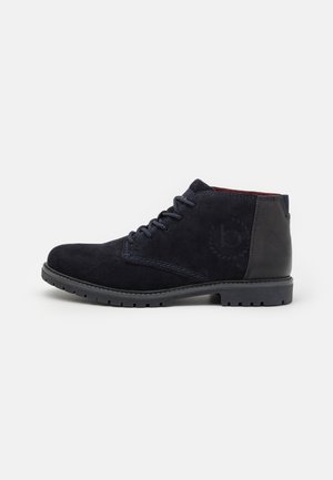 Cizme de gleznă din suede bleumarin cu vârf rotund, design cu șireturi, accente de piele neagră contrastante și talpă din cauciuc texturată pentru aderență.