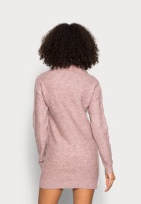 Robe pull en rose doux avec un col roulé et des manches longues, présentant une coupe décontractée et des détails côtelés au niveau de l'ourlet.