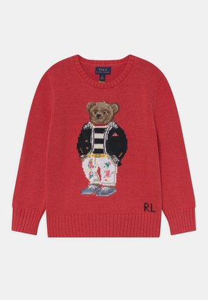Pull rouge en laine tricoté avec un ours portant une chemise rayée, une veste noire, un pantalon fleuri et des chaussures bleues, avec les initiales "RL" en bas à droite.