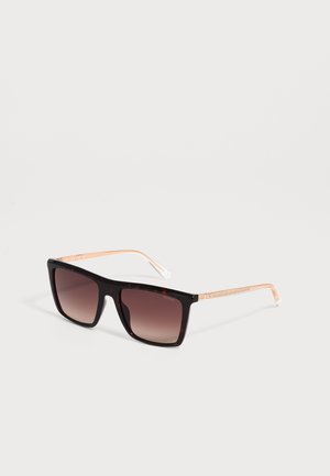 Zwarte zonnebril met vierkante montuur, bruine glazen met verloop en dunne gouden metalen pootjes, liggend op een wit oppervlak.