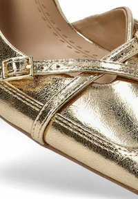 Bailarina metálica dorada con tiras entrecruzadas y detalle de hebilla. Textura de cuero suave y diseño de puntera redondeada.