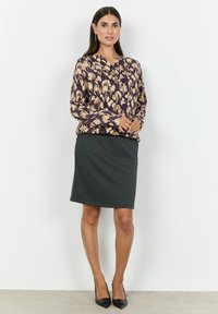 Lila blus med blommönster och långa ärmar, gjord av lätt tyg. Matchad med en figursydd grå pennkjol och svarta klackskor med spetsig tå.