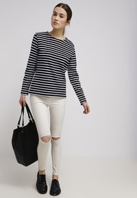 Sort og hvid stribet langærmet top, cremefarvede ripped skinny jeans, sort tote bag og sorte snørebåndssko. En simpel og afslappet påklædning.