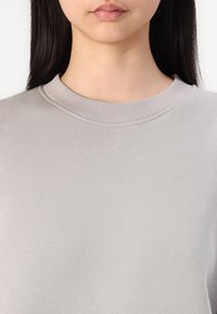 Lys grå genser med rund hals og en glatt tekstur samt ribbestrikket krage. Enkelt design uten mønstre eller merkbare detaljer.