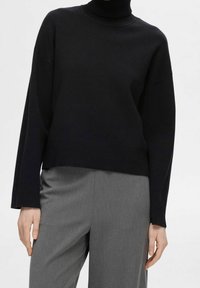 Zwarte coltrui met een relaxte pasvorm, met geribbelde structuur aan de kraag en manchetten. Gecombineerd met grijze, op maat gemaakte broek.