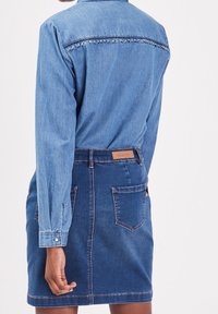 Niebieska sukienka koszulowa z denimu, z kołnierzem zapinanym na guziki, długimi rękawami oraz paskiem w talii z falbaną z tyłu.