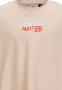 Licht perzikkleurig t-shirt van zachte stof met een ronde hals. Bevat de tekst "HAPPINESS MATTERS RETOUR" in wit en oranje.