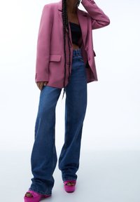 Blazer oversize fuchsia, crop top noir, jean bleu taille haute, et talons compensés roses, avec une texture lisse et une coupe ajustée.