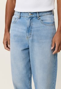 Ανοιχτό μπλε τζιν παντελόνι με κανονική εφαρμογή, πέντε τσέπες, εμπρόσθιο κλείσιμο με κουμπιά και απαλή ξεθώριαση στην υφή του υφάσματος.