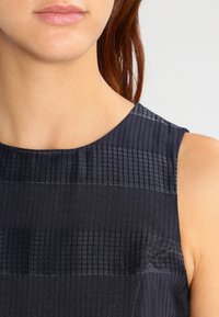 Mörkblå ärmlös topp med ett strukturerat mönster av horisontella ränder. Har en rund halsringning och slät tyg.