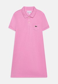 Růžové polo šaty s límečkem, krátkými rukávy a kapsičkou na levé straně hrudníku s zeleným logem Lacoste. Hladký materiál a klasický střih.