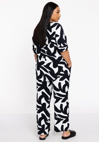 Schwarz-weiß gemustertes Outfit mit einem lockeren Hemd und weitem Hosenbein, aus leichtem Stoff mit einer glatten Textur gefertigt.