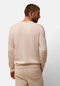 Hellbeige gestrickter Pullover mit langen Ärmeln und runder Ausschnitt, mit gerippten Bündchen und Saum. Getragen mit strukturierten beigen Cordhosen.