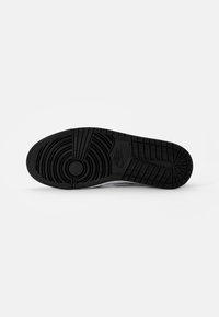 Semelle en caoutchouc noir d'une chaussure de sport avec des motifs de bande de roulement circulaires et en grille, affichant le logo Nike près du centre.