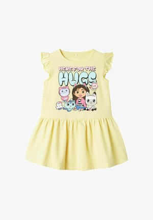 Żółta bawełniana sukienka z krótkimi falbaniastymi rękawami, rozkloszowaną spódnicą oraz centralnym wzorem z postaciami z kreskówek i napisem "TUTAJ DLA UŚCISKÓW."
