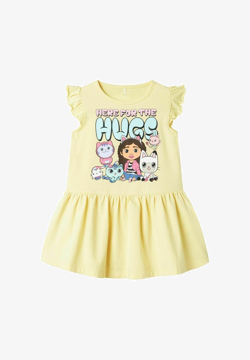 Żółta bawełniana sukienka z krótkimi falbaniastymi rękawami, rozkloszowaną spódnicą oraz centralnym wzorem z postaciami z kreskówek i napisem "TUTAJ DLA UŚCISKÓW."