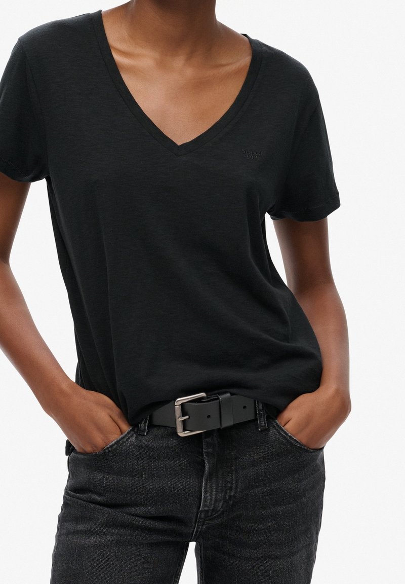 Black V-neck t-shirt made of soft fabric. Features short sleeves and a subtle logo. Paired with dark jeans and a black belt, emphasizing a casual look.