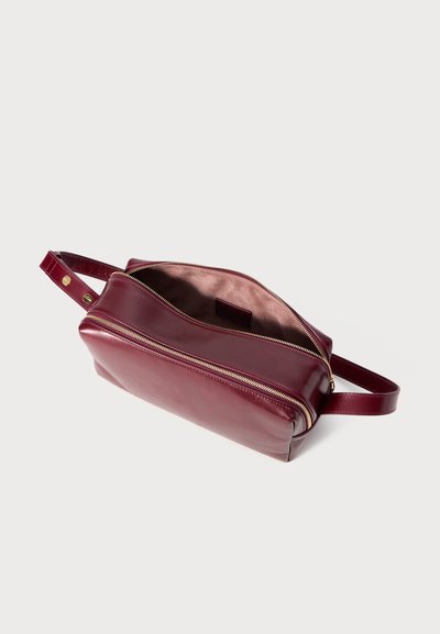 Taisnstūra formas bordo ādas crossbody soma ar zelta rāvējslēdzēju, plašu jostu un atvērtu augšpusi, kas atklāj gludu satīna iekšējo oderi.