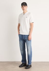 Hvit kortermet polo skjorte med glidelås, svart logo; lyseblå rett ben denim jeans; svarte sneakers; svart caps med logo.