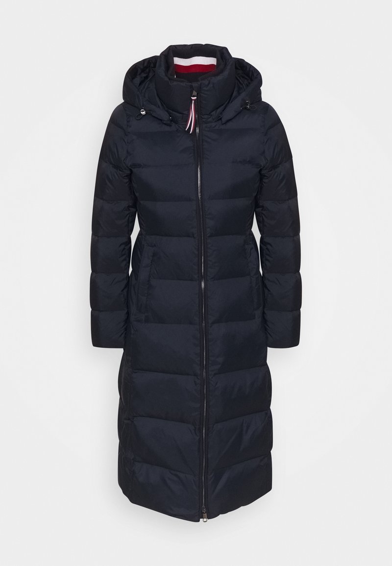 Abrigo acolchado en azul marino oscuro con capucha, que presenta un cierre de cremallera, diseño acolchado y mangas ligeramente abombadas. El interior del cuello tiene rayas rojas y blancas.