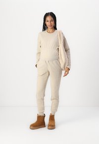 Sweat-shirt beige et joggeurs assortis avec une taille à cordon. Texture douce. Bottes ankle marron avec une semelle épaisse et une doublure en fourrure.