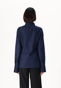 Tumman denim-takki pitkillä hihoilla, slim fit -designilla, terävällä kauluksella ja napillisilla hihansuilla. Puhtaat linjat ilman näkyviä kuvioita tai korostuksia.