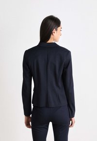 Marineblazer med skreddersydd passform, notched lapels og lange ermer. Glatt stoff med minimale sømmer og en litt utsvakt bak.