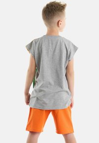 Camisa gris de manga corta con acentos coloridos en los hombros, combinada con pantalones cortos naranjas. La camisa tiene un corte relajado y una textura suave.