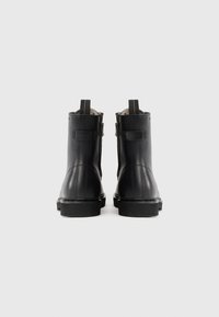 Botas de tobillo de cuero negro con textura suave, que cuentan con cremalleras laterales, tiradores y una suela de goma resistente.