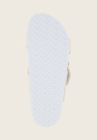 Ljusbeige sandal med en texturerad vit gummisula, med ett vågigt mönster. Justerbar rem på sidan med en metallspänne.