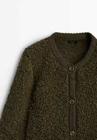 Olijfgroene, textuurvolle cardigan van een zachte, pluizige stof. Voorzien van een ronde halslijn, knoopsluiting en gebreide accenten langs de randen.