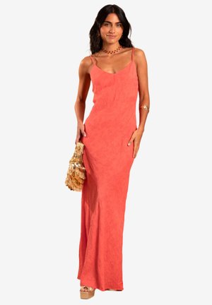 Koraal maxi-jurk met spaghettibandjes, gestructureerde stof, getailleerde silhouette en zijsplit, in combinatie met een bewerkte gouden handtas.