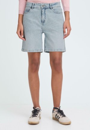 Jeansshorts in Hellblau mit hohem Bund, klassischem Fünf-Taschen-Design und umgeschlagenen Säumen, kombiniert mit schwarzen und beigen Turnschuhen.