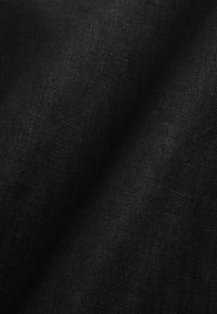 Gros plan sur une texture de tissu noir tissé avec un motif de tissage visible et des plis subtils créant des ombres douces.