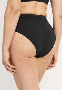 Högmidjade svarta underkläder med slät tyg, sömlösa kanter och klassisk snitt, som visar diskret täckning baktill och en minimalistisk design.