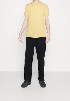 Gul polo t-shirt med et sort logo, parret med sorte corduroy bukser og mørke sneakers. Pasformen er afslappet med korte ærmer.