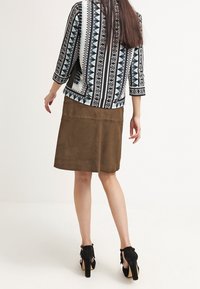 Zwart-wit gestreepte jas met 3/4 mouwen over een bruine suède rok. Zwarte hakken met gouden accenten maken de outfit compleet.