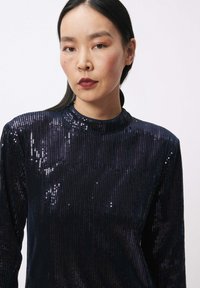 Zwart pailletten top met lange mouwen en hoge hals, met een aansluitend ontwerp en een gladde textuur, wat een glinsterend effect creëert.