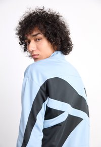 Light blue and black jacket with a smooth texture featuring a geometric design. Distinctive color blocking and a high collar.