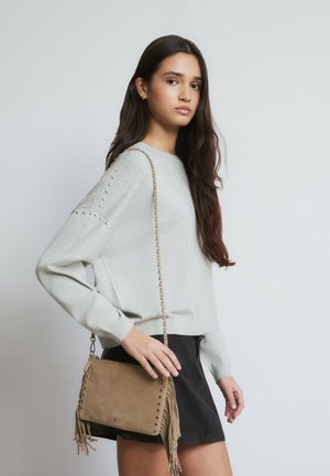 Jersey gris claro de manga larga con detalles de tachuelas en los hombros, combinado con un bolso cruzado de ante color marrón claro con detalles de flecos.