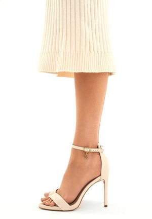 Nude-nuoraiset korkokengät yksinkertaisella muotoilulla, jossa on ohut nilkkastrappi, nauhatossun solmikohta varpaassa ja kultaketju strapissa.