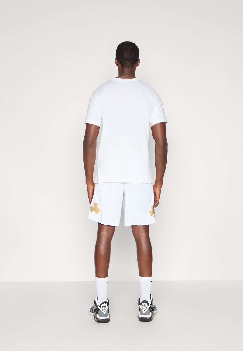 White cotton t-shirt and white shorts with gold clover accents, paired with black sneakers and white socks, viewed from behind.
